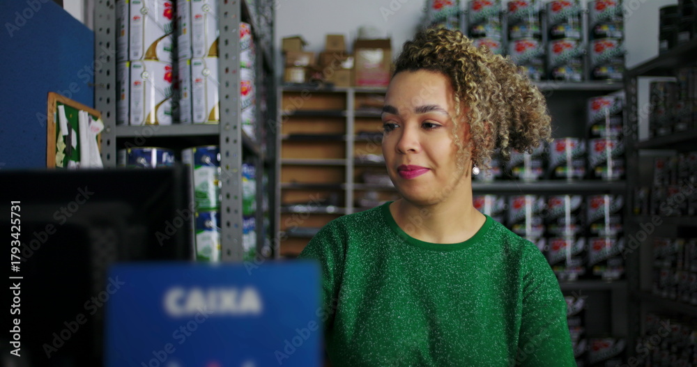 Obraz premium Young woman working on a computer at a desk in a hardware store, smiling and focused, surrounded by shelves of products in a professional retail setting