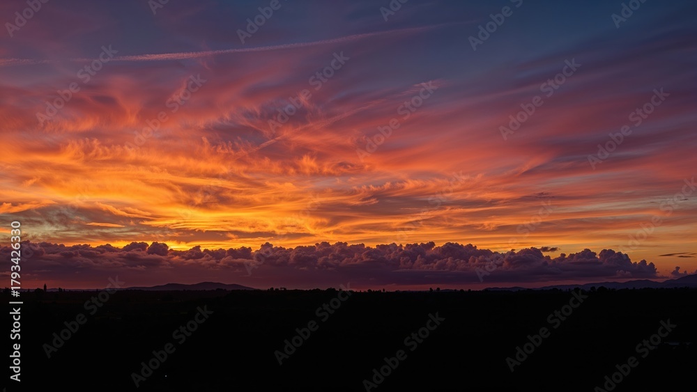 Fototapeta premium Vivid sunset sky with orange, pink, and purple hues over a dark landscape.