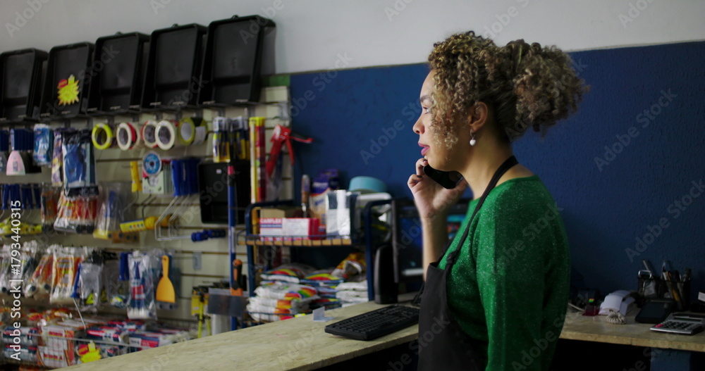 Obraz premium Dedicated shopkeeper on a phone call at the counter in a hardware store, surrounded by tools and supplies, managing tasks with professionalism and focus
