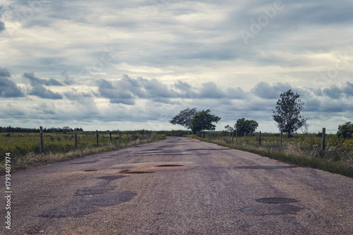 Rural road with potholes under cloudy sky