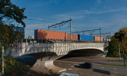 Moving freight train loaded with shipping containers crossing elevated railway bridge (this image was made with an anamorphic lens)