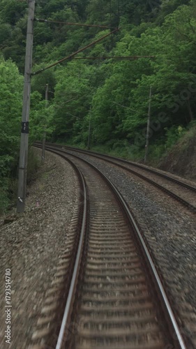 A first-person view of train tracks curving through a green forest from a moving train. This dynamic shot evokes a sense of speed and journey. Perfect for travel vlogs or transport themes.