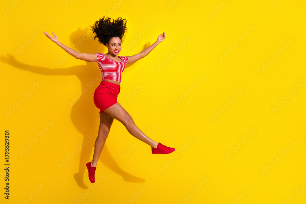 Φωτογραφία Joyful young woman in vibrant casual outfit leaps mid-air against a bright yello