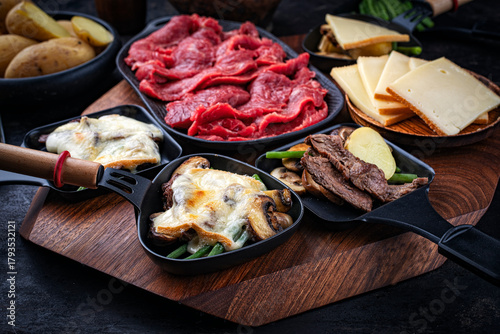 Traditional authentic Swiss raclette with beef meat, boiled potatos, green beans and mushrooms served as close-up on a wooden design board
