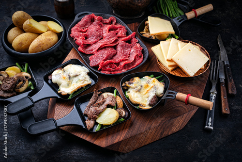 Traditional authentic swiss raclette with beef meat, boiled potatos, green beans and mushrooms served as close-up on a wooden design board