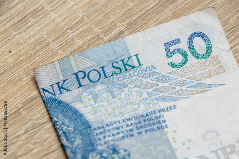 Obraz premium Close-up of a Polish 50 zloty banknote featuring intricate details and the word 'Bank Polski' on a wooden surface, representing currency and finance.