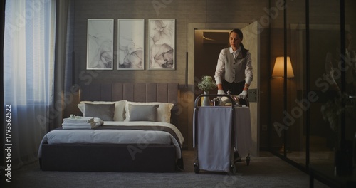 Hotel Maid Entering Elegant Hotel Room With Breakfast Trolley. in Cozy Interior With Stylish Decor, Woman Places Breakfast Cart Next Bed. Guest Care, Professional Hotel Service Routine. Static Shot.