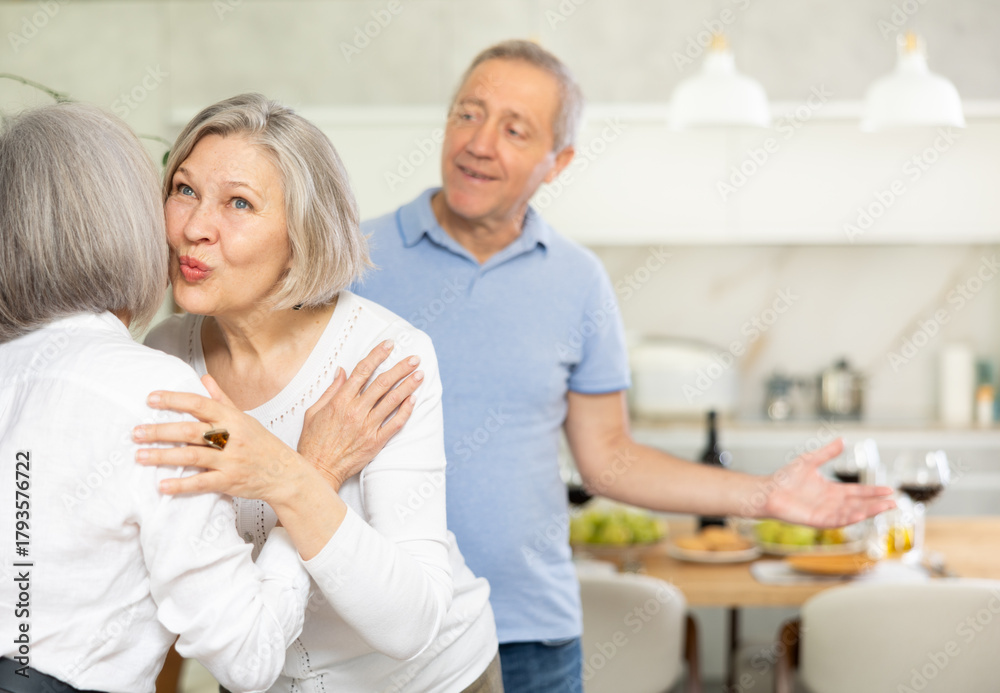 Fototapeta premium Two elderly women friends hugging in kitchen at home