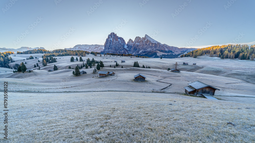 Fototapeta premium Alpe di Siusi, Italy - Panoramic view of wooden cottages and yellow larches at Seiser Alm, freezy morning sunrise, at Dolomite plateau in South Tyrol province in the Dolomites Alps