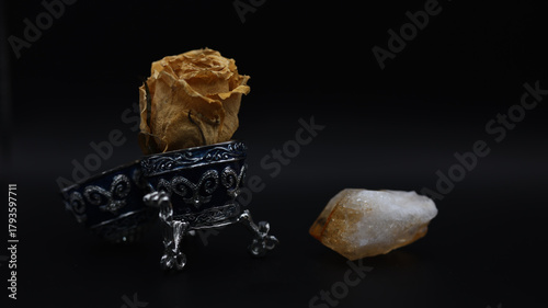Fading and Eternity. Dried Rose Bud in Ornate Metal Holder Beside Glowing Crystal on Dark Background