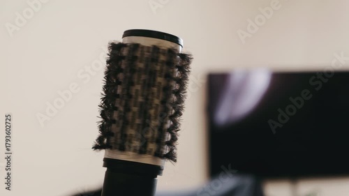 close-up round hair brush on vanity, soft warm lighting, blurred monitor background, textured bristles, professional styling tool, calm morning