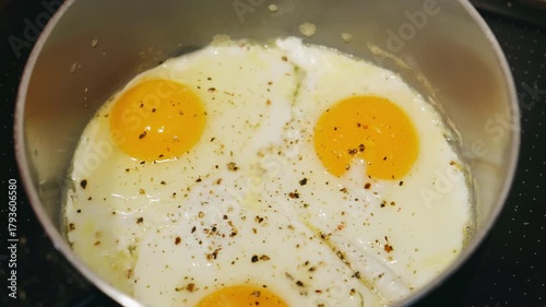 fried eggs in pan with pepper and salt, gently sizzling on stovetop, bright golden yolks, set whites, light seasoning, cozy kitchen morning, homemade