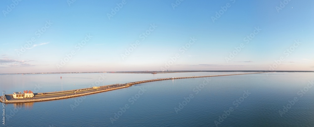 Fototapeta premium Aerial View Of Long Monitor Merrimac Memorial Bridge Tunnel crossing tranquil blue water of Hampton Roads Channel with a distant harbor and open sky
