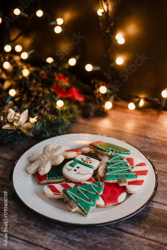 Christmas cookies on plate with golden lights on rustic table. Baking traditional snowman, tree, star cookies and santa hat for holidays 