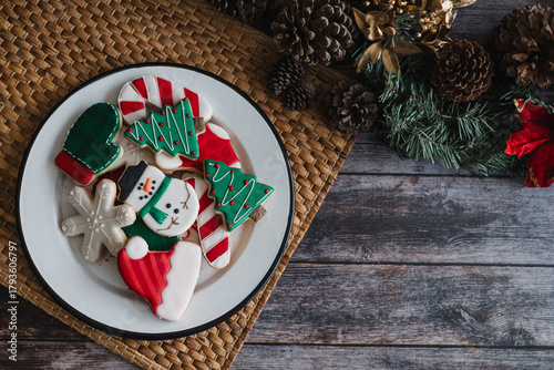 Christmas cookies on plate with golden lights on rustic table. Baking traditional snowman, tree, star cookies and santa hat for holidays 