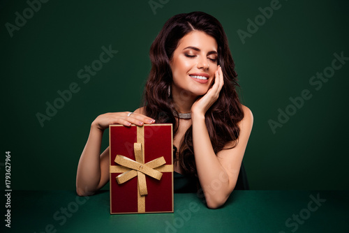 Stunning young brunette woman holding a beautifully wrapped gift box, posing with a glamorous smile