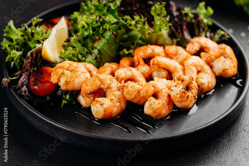 Grilled shrimp salad with mixed greens, cherry tomatoes and lemon on a black plate