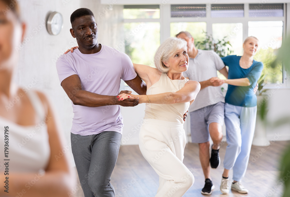 Fototapeta premium Active mature men and women practicing Rock 'n' Roll dance in training hall during dancing classes