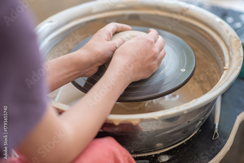 Close-up of a potter's hands centering a lump of wet clay on a spinning wheel. Focused, hands-on artistic process for craftsmanship, education, and ceramic art.