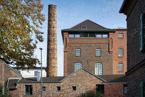 Preserved industrial red brick architecture (former SesterKoelsch  Brewery, 1904) with a prominent chimney, repurposed as modern residential housing in Cologne, Germany