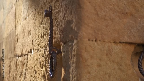 Wrought iron horse tie rings on old stone building wall. Close-up view of antique wrought iron horse tie-up rings with decorative details, attached to the weathered stone block wall