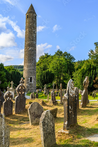The iconic 11th-century Round Tower stands tall over the ancient Celtic crosses and grave markers in the monastic city of Glendalough.