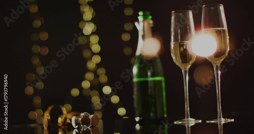 Champagne bottle and two flutes shifting into focus after bright flare, emphasizing festive mood