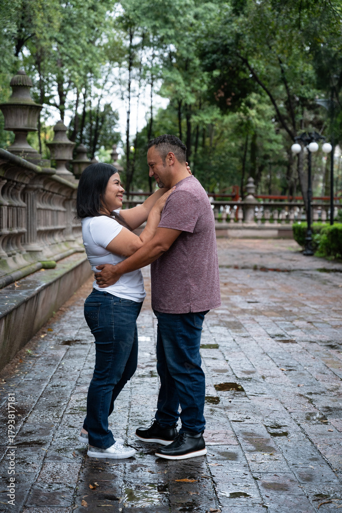 Fototapeta premium Smiling couple sharing tender moment in city park after rain