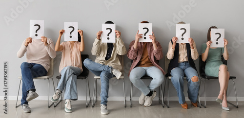 Applicants holding paper sheets with question marks near light wall