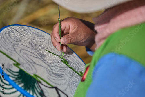 The weathered hands of an Uros elder skillfully guide a crochet needle through vibrant threads, preserving generations of ancestral craftsmanship.