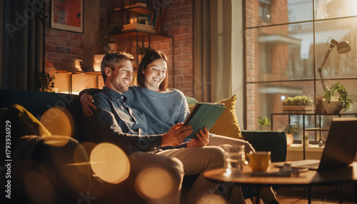 Wallpaper Mural Happy couple sitting on cozy sofa in modern living room, smiling while checking investment portfolio on digital tablet, warm evening light, relaxed atmosphere Torontodigital.ca