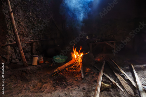 Cooking fire blazing smoking inside African villagers hut by wooden table and basic furniture in Gasure Rwanda.