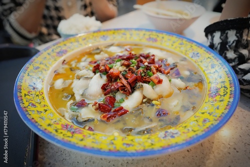 Close-up ceramic bowl filled with spicy Szechuan Chinese fish dish called Suan Cai Yu, Sichuan Pickled Vegetable Fish or Shui Zhu Yu , Sichuan Boiled Fish. Heavily topped of dried red chili peppers.