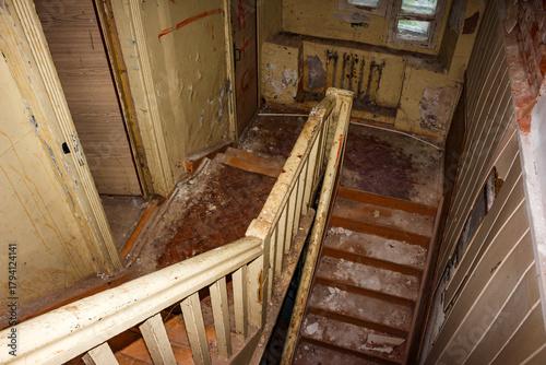 Haunting abandoned building interior with a dilapidated wooden staircase. Peeling paint and grimy debris on steps show urban decay, historical neglect, and forgotten architecture