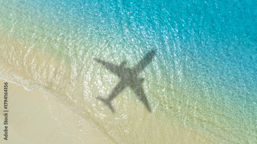 Obraz premium Aerial view of shadow passenger plane silhouette and sandy beach blue sea with waves at sea beach summer vacation sea travel concept