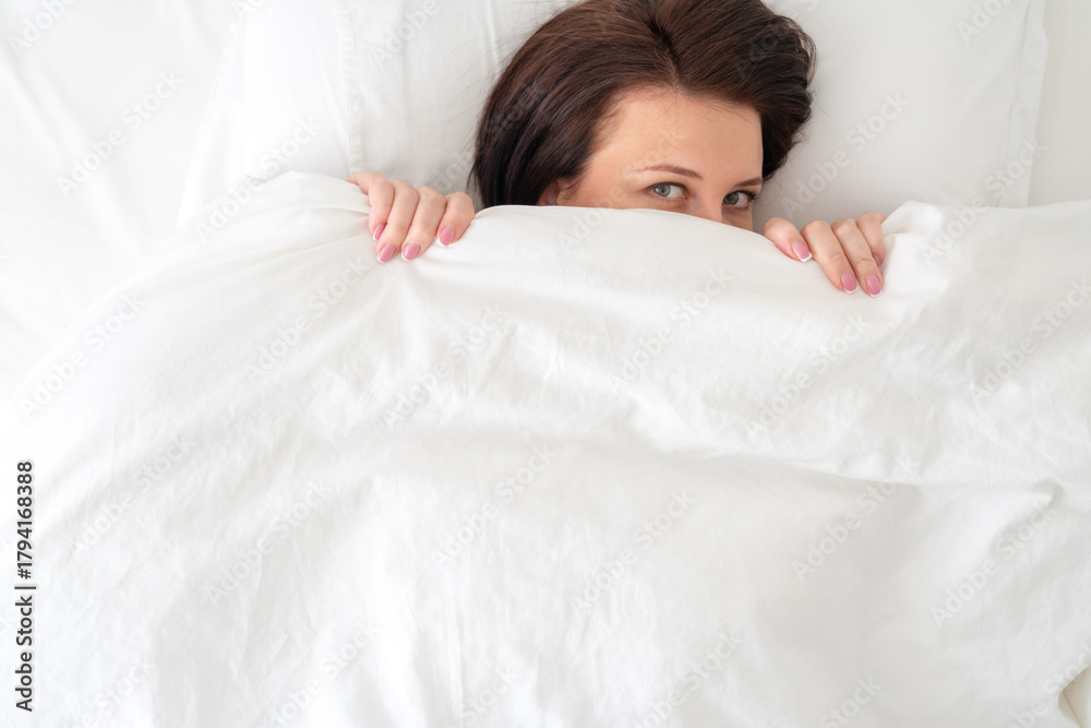 Obraz premium Portrait of young beautiful woman in bed covered with blanket