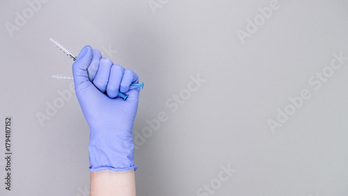 Hand in blue gloves of doctor or nurse holding syringe with liquid vaccine over grey background with copy space. New vaccine. Unknown vaccine. Medical gloves.