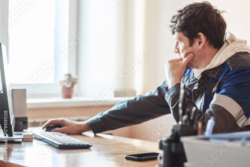 A focused man sitting at a desk, working on a computer in a bright office. The setting conveys productivity and concentration.