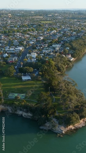 Aerial view of a residential area on a peninsula in Point Chevalier, Auckland, New Zealand. Houses are nestled among trees, with a park visible on the peninsula's tip.