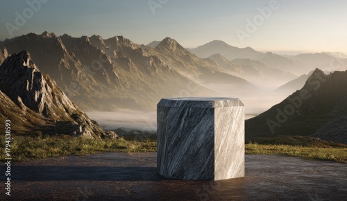 A large, gray, marble-like pedestal stands prominently in the foreground, with a stunning mountain range and a misty valley stretching out into the distance under a bright sky