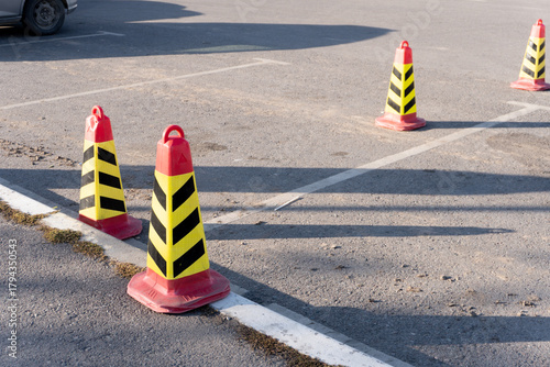 Several red and yellow striped traffic cones are arranged in an empty parking lot. The cones are placed to block off certain parking spaces on the asphalt surface.