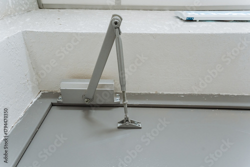 metal door closer with hydraulic and hinge details, inspectionfocused image of door closer and mounting bracket, detailed view of hydraulic mechanism and hinge assembly on commercial building door