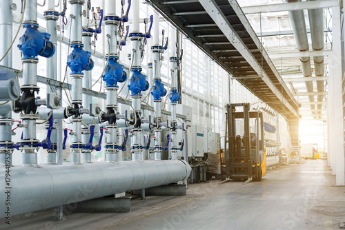 Large industrial water treatment and boiler room. Shiny steel metal pipes and blue pupms and valves.