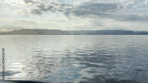 Serene Tranquility: Calm Waters Reflecting Sunlit Clouds with Majestic Mountains in the Background. HDR Video, Seamless Loop