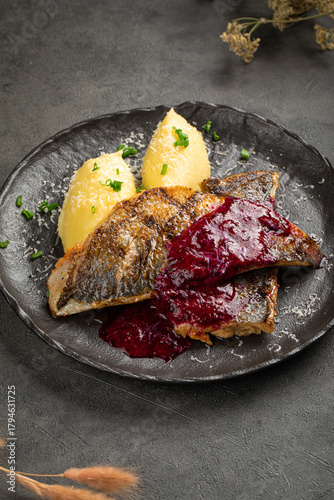 Fried fish fillet served with mashed potatoes and beet sauce on black plate over dark background