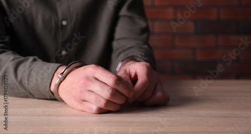 Fotografía Man in handcuffs at wooden desk indoors, closeup. Space for text