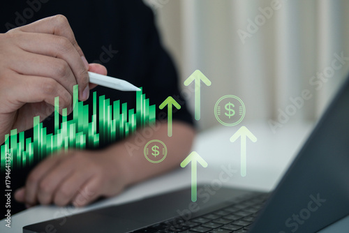 Stock market investment and financial growth concept. A person's hand uses a stylus to analyze a green candlestick chart on a virtual interface, showing rising trends, arrows, and dollar signs.
