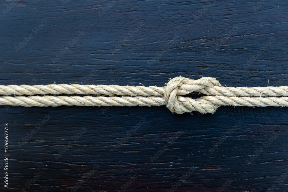 Fototapeta premium Tied rope knot on dark wooden background, symbolizing unity, strength, security, and resilience. Great for business, relationship, or nautical concept visuals and design projects.