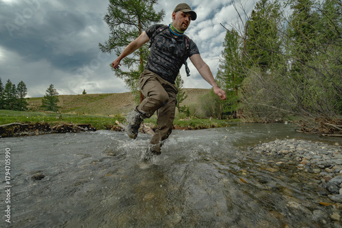 Obraz na plátně A traveler runs through a mountain stream on a green meadow in the Altai steppe