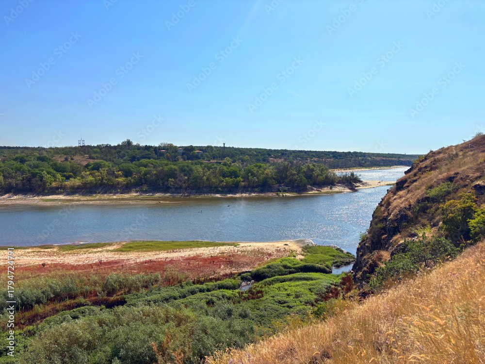 Obraz premium Amazing panorama of the Dnieper riverbed surrounded by dense thickets of sedge and reeds, washing the island of Baida, against the background of a sunny summer sky.